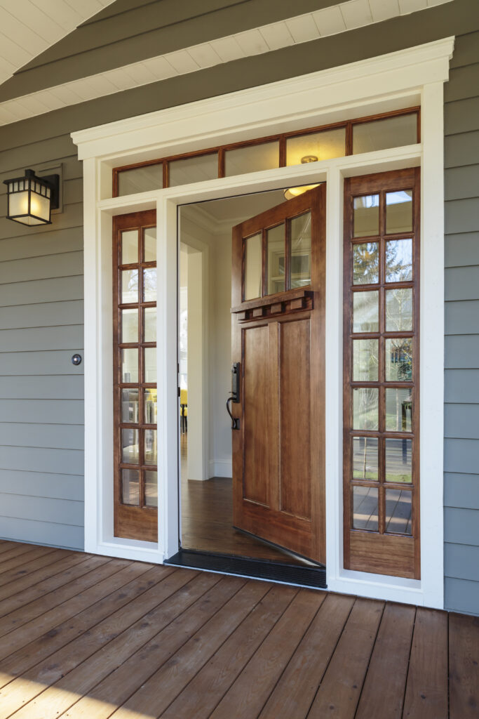 Front door open on the front porch of a grey house.